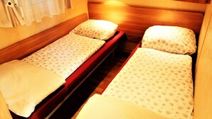 A small, cozy room with two single beds, wooden headboards, and a small window with curtains. - Stacaravan Rozika Slowenien by Interhome (Slovenj Gradec)