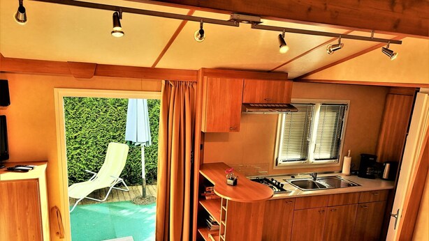 A compact kitchen with wooden cabinets, a sink, and a window. - Stacaravan Rozika Slowenien by Interhome (Slovenj Gradec)