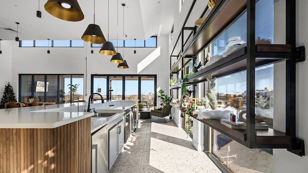 Une cuisine moderne dotée d’un grand îlot central, de luminaires suspendus et de grandes fenêtres offrant une vue sur la ville.
