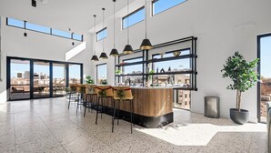 Une cuisine moderne dotée d’un îlot central, de tabourets de bar, de luminaires suspendus et de grandes fenêtres offrant une vue sur la ville.