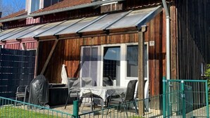 A wooden house with a covered patio area, a fenced yard, and a number 55 sign. - Wohlfühlhaus 55 by Interhome (Zandt)