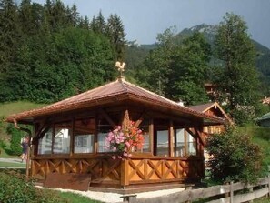 Eine Holzhütte mit geneigtem Dach, großen Fenstern und einem Blumenarrangement davor.