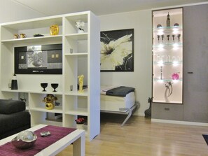 Een moderne woonkamer met een witte tv-meubel, een bank, een salontafel en een glazen vitrinekast met decoratieve objecten.