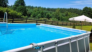 A rectangular above-ground pool with a ladder, surrounded by a wooden fence and lush greenery.