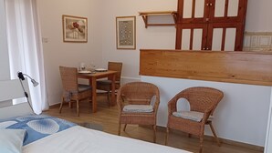 A bedroom with a bed, a desk, two wicker chairs, a wooden cabinet, and a wall-mounted shelf.