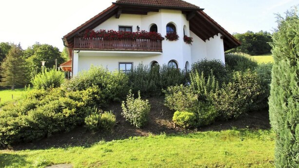 Una casa a due piani con un balcone, immersa nel verde.