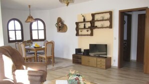Un soggiorno con un divano, un tavolino da caffè con un cesto di frutta, una TV su un mobile in legno e un'area pranzo con tavolo e sedie.