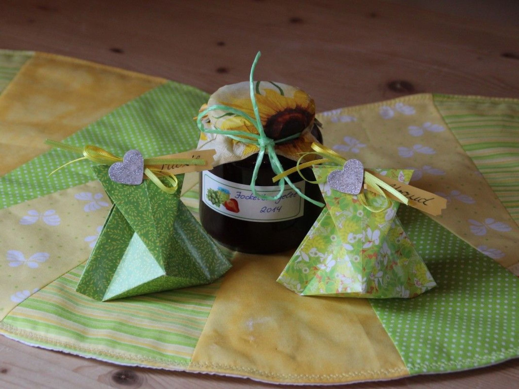 A bottle of wine with a label, two small gift bags, and a decorative item on a tablecloth.