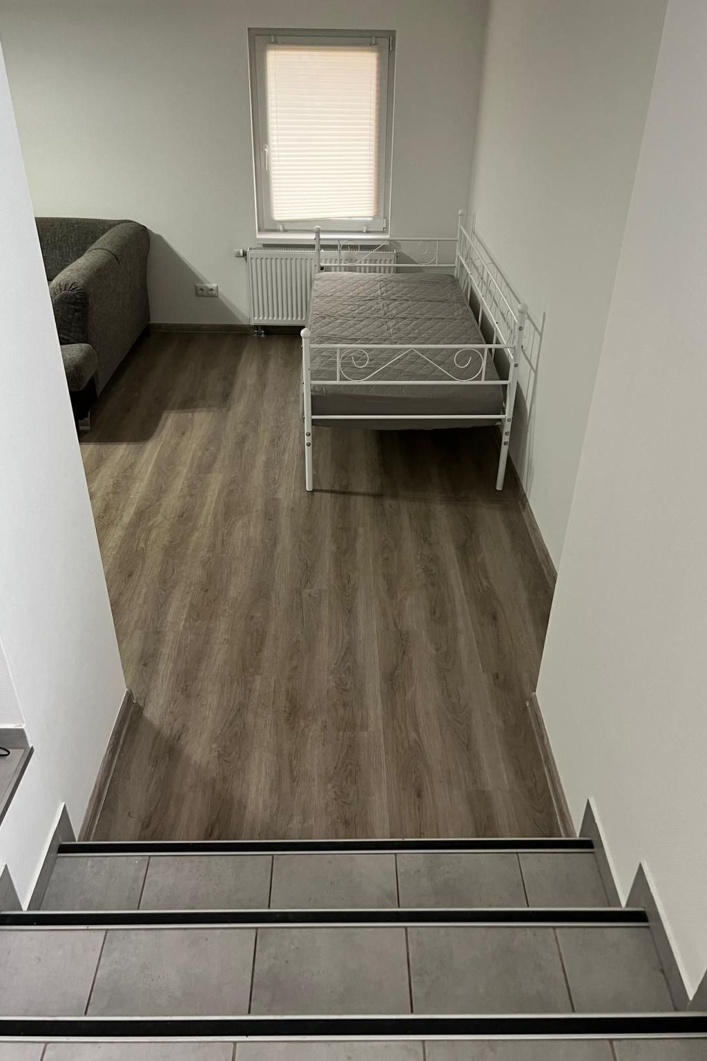 Een kamer met een bed, een radiator, een raam en een bank.