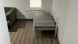 Ein Zimmer mit Bett, Heizkörper, Fenster und einer Couch.