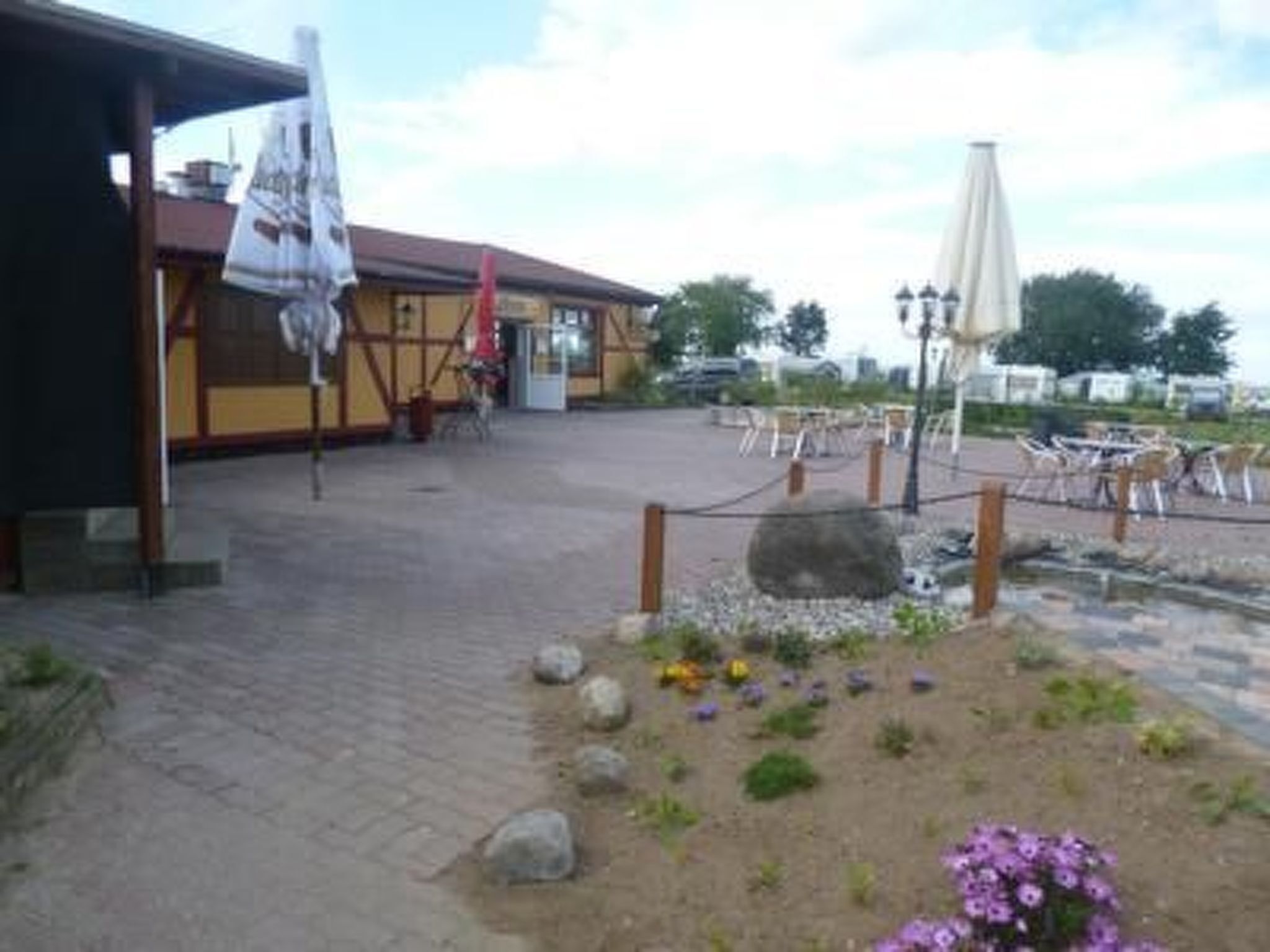 Ein Außenbereich mit Tischen und Stühlen, ein überdachter Sitzbereich und ein Garten mit Steinen und Blumen.