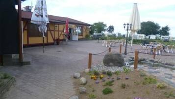 Ein Außenbereich mit Tischen und Stühlen, ein überdachter Sitzbereich und ein Garten mit Steinen und Blumen.
