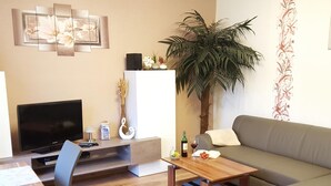 A living room with a flat-screen TV, a wooden coffee table, a sofa, a dining table with chairs, and a decorative plant. - Ferienwohung 1 - Erdgeschoss by Interhome (Zempin)