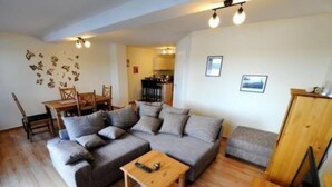 A living room with a sofa, a coffee table, a TV stand, and a dining area with chairs and a table. - Apartment Karpfen 4 by Interhome (Neukloster)