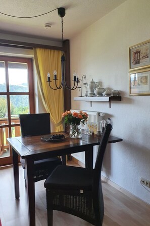 Zona pranzo con tavolo in legno, sedie, un lampadario, un vaso con fiori e una mensola con teiere.