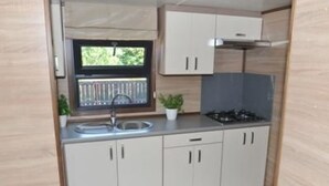 A compact kitchen with a window, a sink, cabinets, and a stove. - Mobilheim Zweiundvierzig in Lychen by Interhome (Lychen)