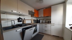 Eine kleine Küche mit weißen und orangefarbenen Schränken, einem eingebauten Ofen und einer Kaffeemaschine.