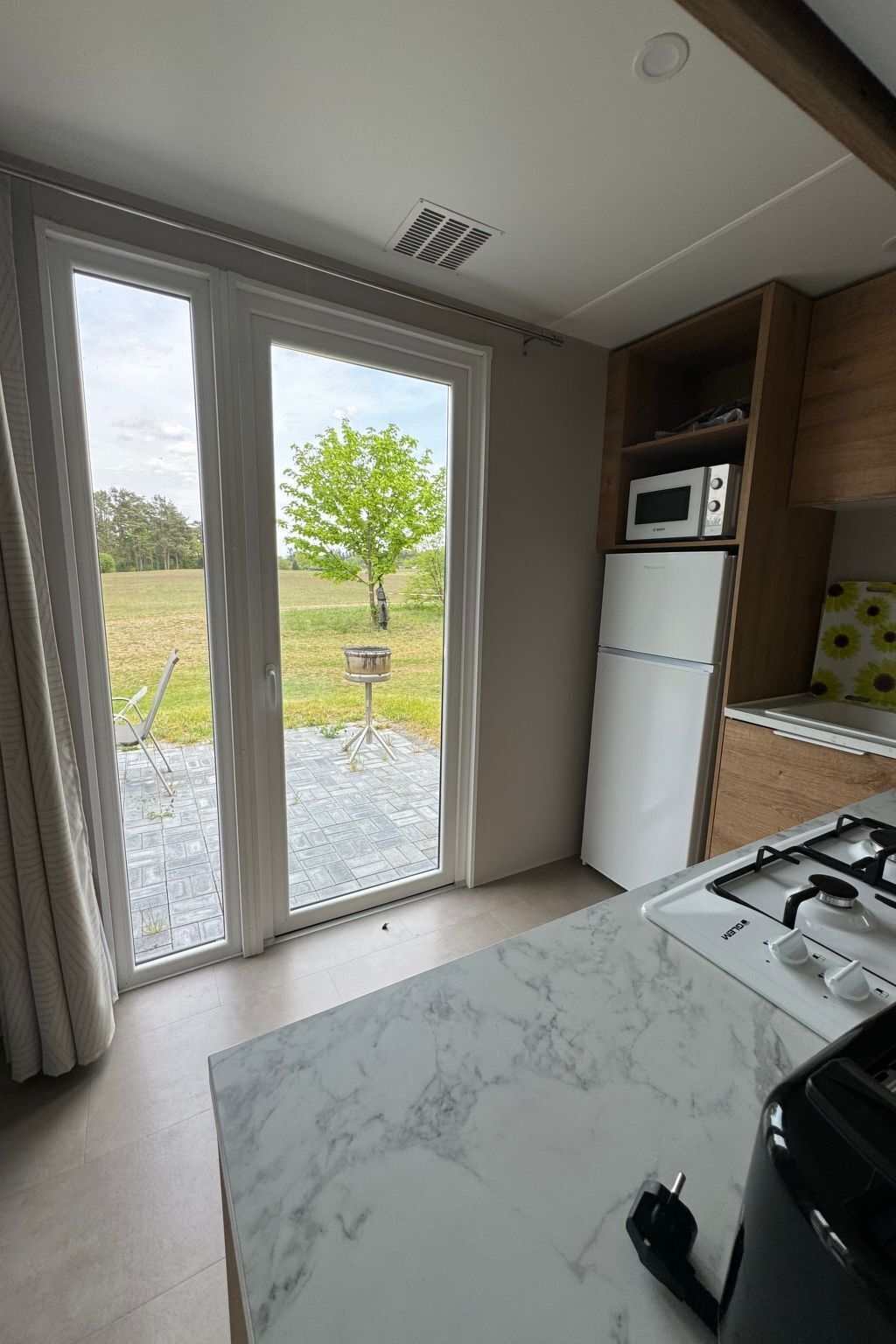 Une cuisine moderne équipée d’une cuisinière à gaz, de meubles blancs et d’une porte-fenêtre coulissante donnant sur un patio.