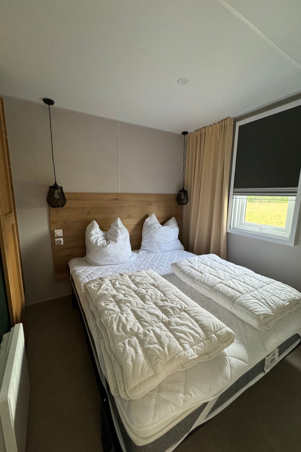 Et hotelværelse med en seng, et vindue med gardiner og en træsenggavl.