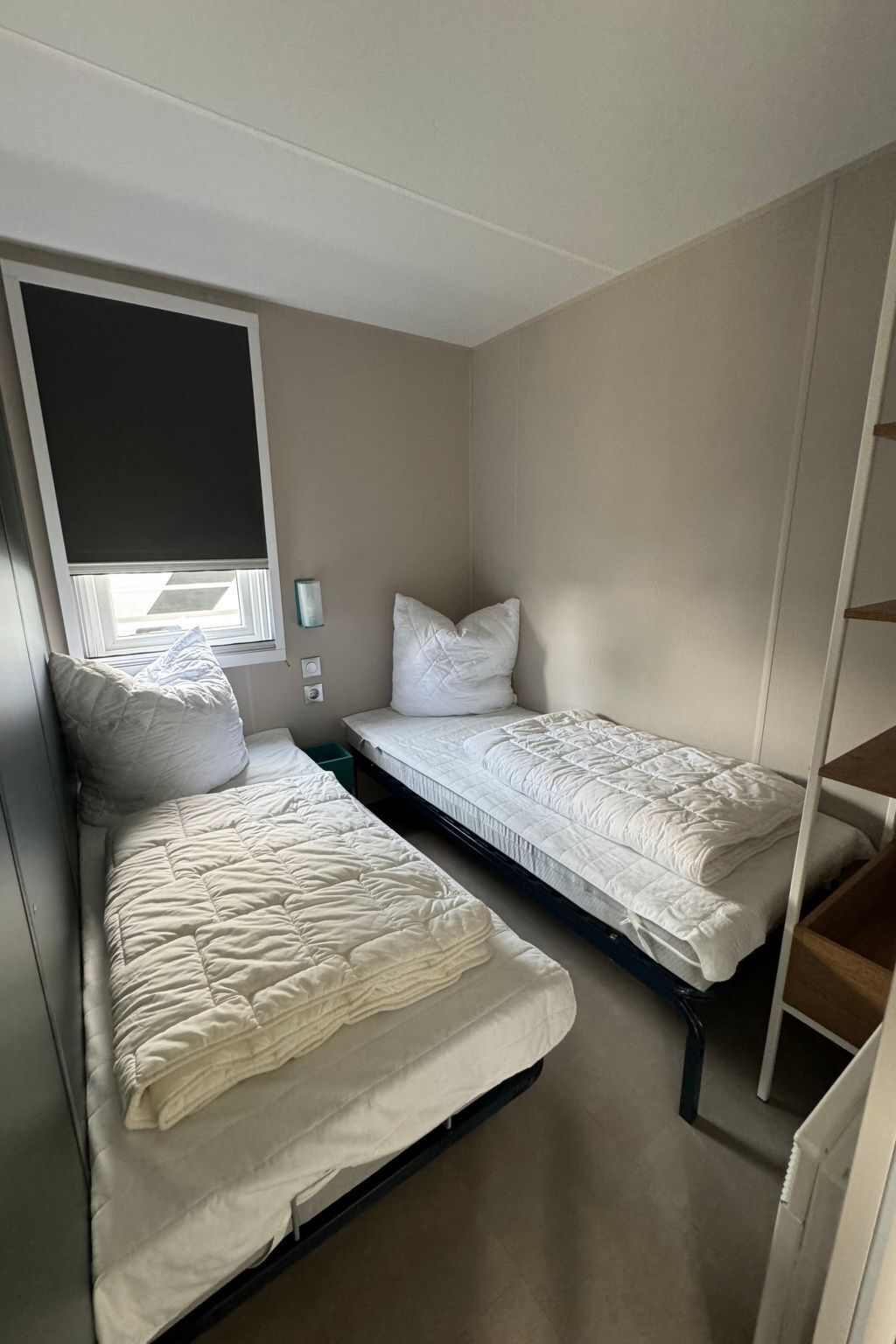 A bedroom with two beds, a window with a blind, and a built-in shelf.