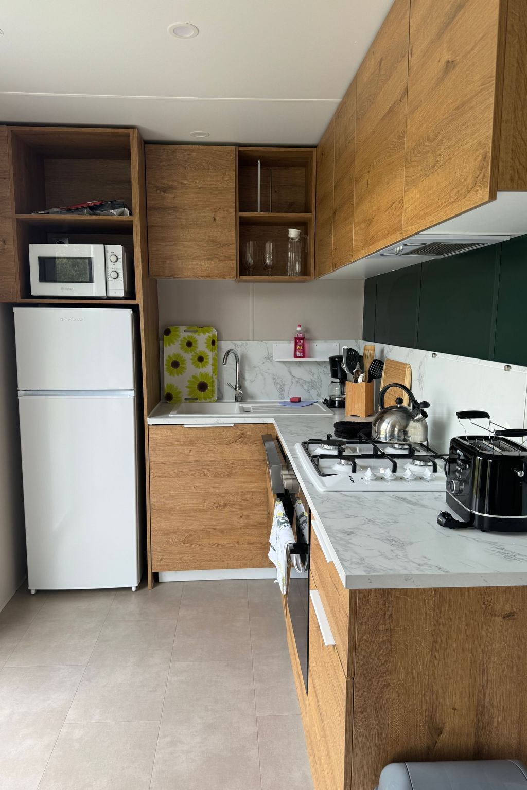 Cuina moderna amb armaris de fusta, un refrigerador blanc, un microones, una cuina de gas i un rentaplat.