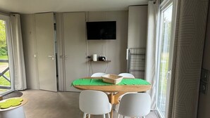 Una habitación moderna con mesa de comedor, sillas, televisión de pantalla plana y un amplio ventanal con cortinas.