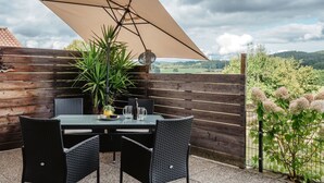 Une terrasse extérieure avec une table et des chaises, un grand parasol et une vue sur la campagne.