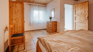 Une chambre à coucher avec un lit en bois, une commode en bois, une chaise et une fenêtre ornée de rideaux légers.