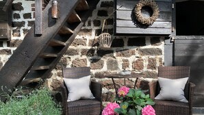 A rustic outdoor seating area with wicker chairs and a potted plant of pink flowers. - Weyerhof by Interhome (Kobern-Gondorf)
