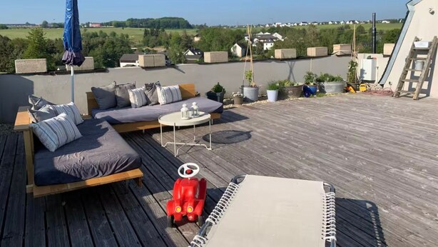 Une terrasse sur le toit avec un canapé, une petite table et une voiture jouet rouge.
