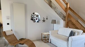 Une chambre de style loft moderne, avec un canapé blanc, un fauteuil en osier, une petite table et une lampe.