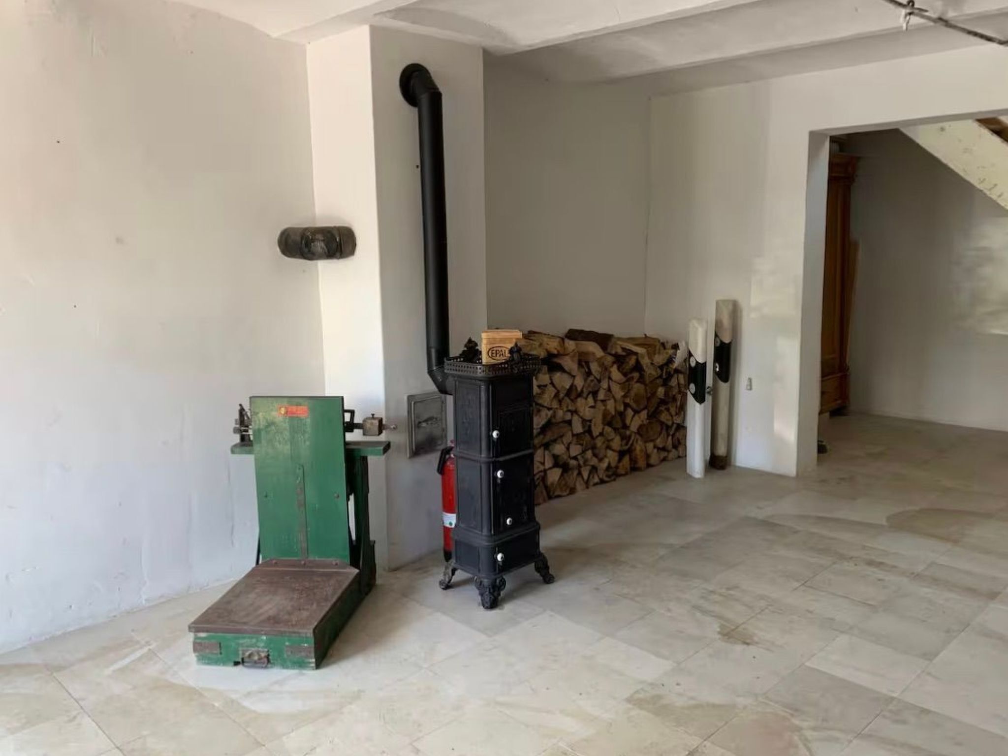 A room with a fireplace, a green heater, and a stack of firewood.