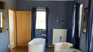 Une chambre moderne avec un plancher en bois, une grande baignoire, un canapé blanc, une petite table ronde et une porte en bois.