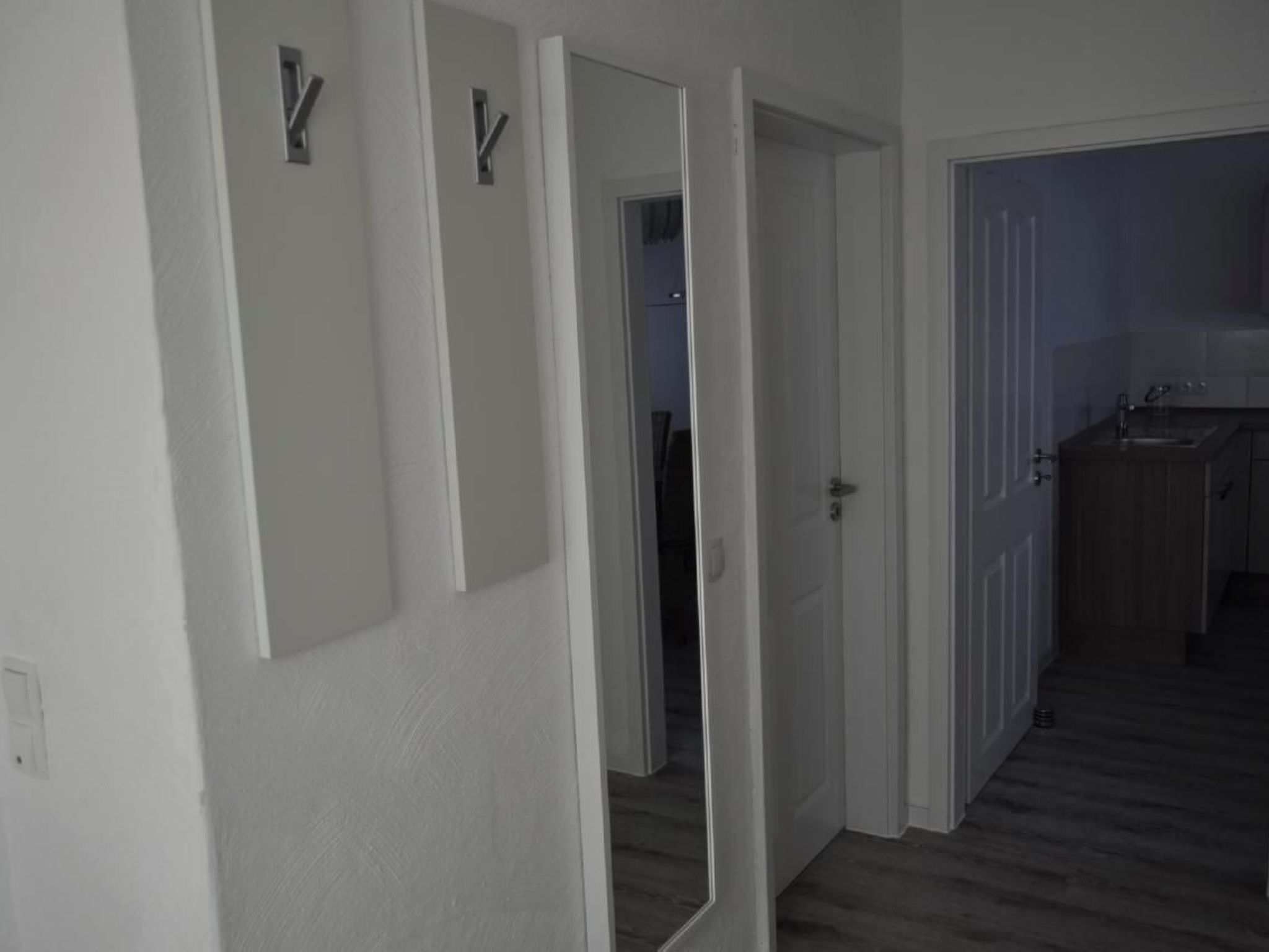 Un couloir aux murs blancs et au plancher en bois qui mène à une cuisine.