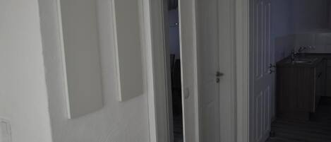 Un couloir aux murs blancs et au plancher en bois qui mène à une cuisine.