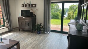 A spacious living room with a large window, a television, a cabinet, and a table. - Ferienwohnung Seeweg 4 by Interhome (Lychen)