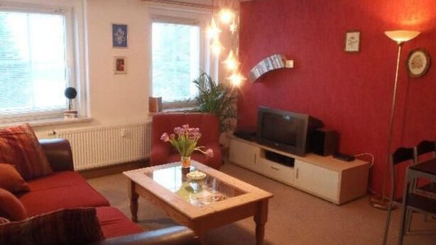 A living room with a red wall, a sofa, a coffee table, a TV, and a floor lamp. - Erzgebirge by Interhome (Johanngeorgenstadt)