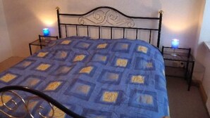 A bed with a patterned blue and yellow bedspread, two bedside lamps, and a metal headboard. - Erzgebirge by Interhome (Johanngeorgenstadt)