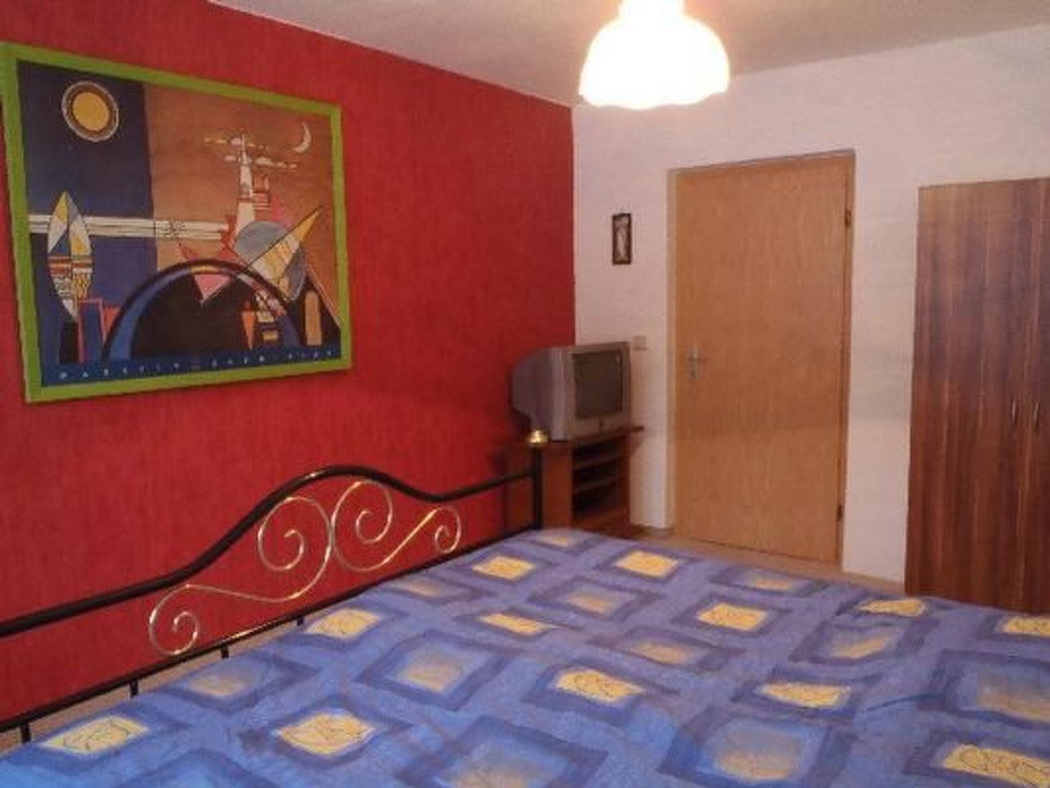 A bedroom with a bed, a television on a stand, a door, and a painting on the wall.