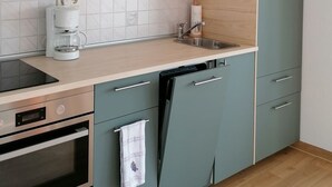 Eine moderne Küche mit türkisfarbenen Schränken, einem eingebauten Backofen, einer Kaffeemaschine und einem Spülbecken.