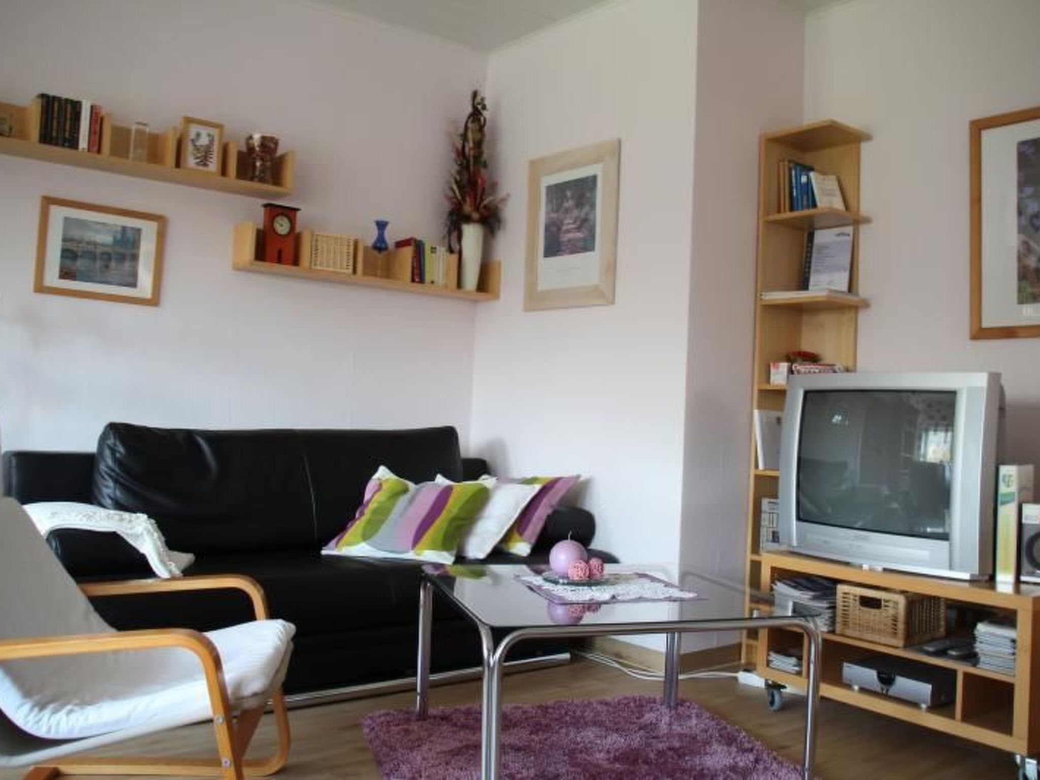 Ein Wohnzimmer mit einer schwarzen Couch, einem Glastisch, einem Holz-TV-Möbel und einem Bücherregal.