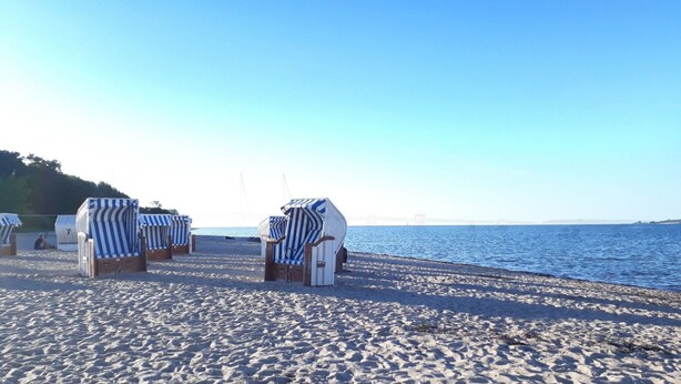 A beach with striped beach chairs and umbrellas, a clear sky, and calm sea. - Vacation home "Henk" by Interhome (Alt Jassewitz)