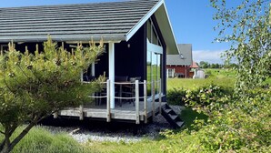 Une cabane moderne dotée d’un porche couvert, d’une terrasse et offrant une vue sur un paysage rural.