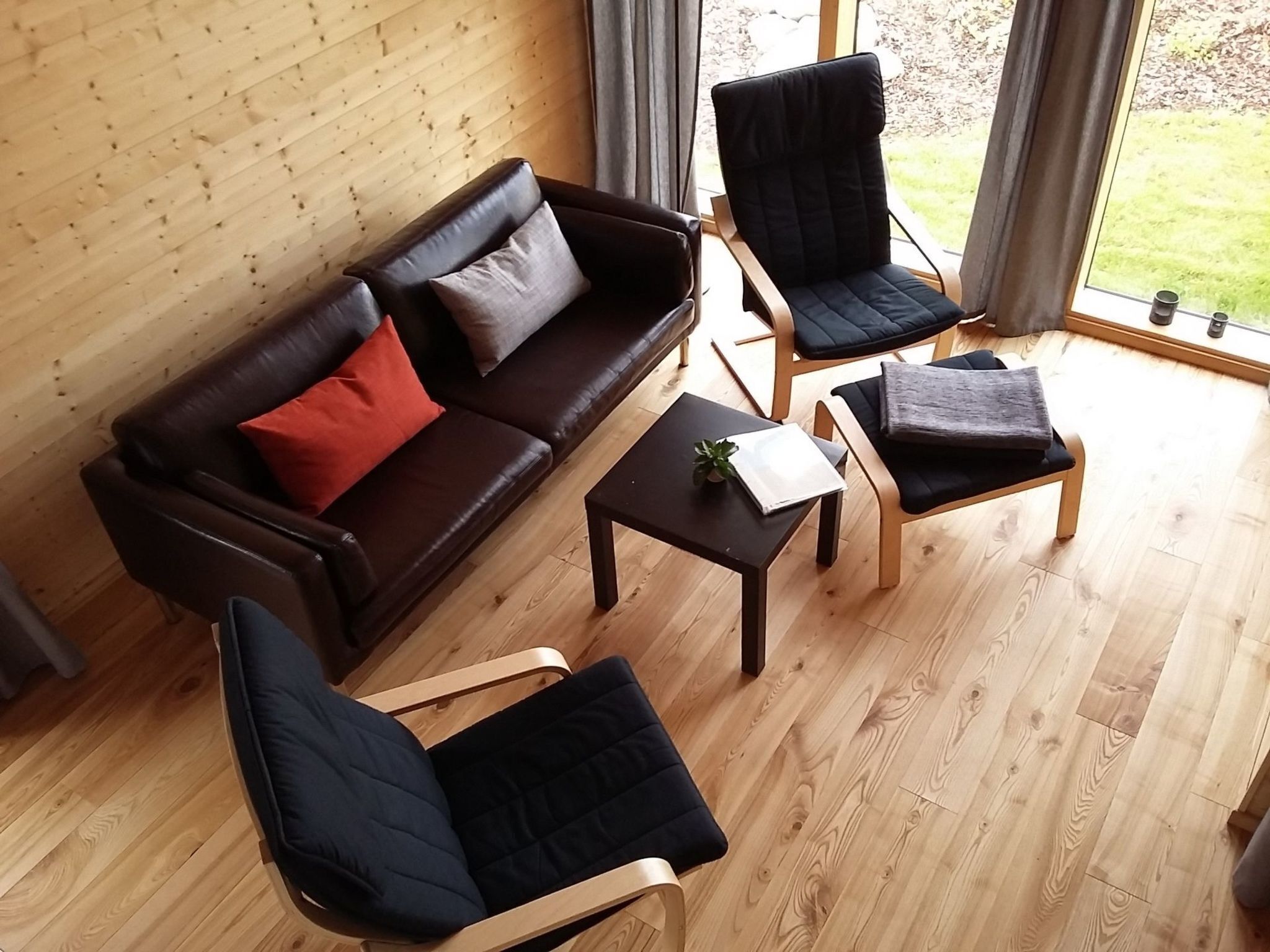 A cozy living room with a dark brown leather sofa, two black armchairs, and a small wooden coffee table.