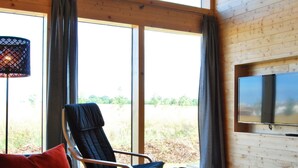 Une pièce avec une grande fenêtre, un fauteuil, un canapé, une table et un téléviseur fixé au mur.
