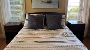 Ein Schlafzimmer mit einem Bett, zwei Nachttischen, einem Bild von einem Boot an der Wand und einem Fenster mit Jalousien.