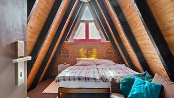 Ein gemütliches Schlafzimmer im Dachgeschoss mit schrägen Wänden, einem Bett mit karierter Bettdecke und einem Fenster mit rotem Rahmen.