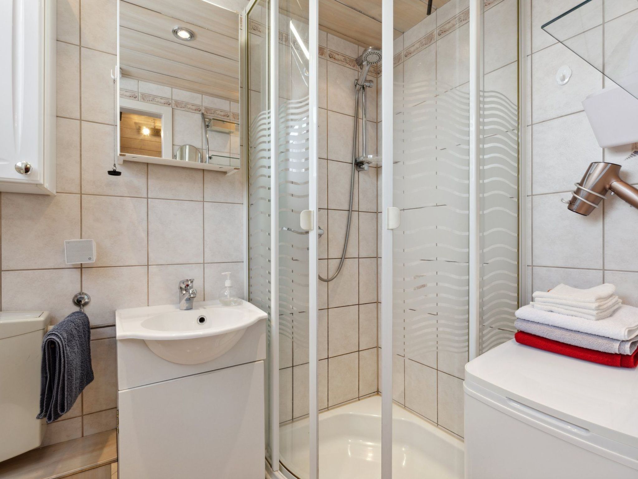 A modern bathroom with a glass-enclosed shower, a sink, and a towel stack.
