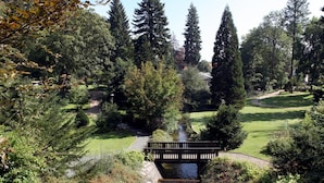 Un parc avec un petit pont enjambant un ruisseau, entouré de grands arbres et doté d’une pelouse bien entretenue.