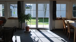 Une pièce lumineuse avec de grandes fenêtres, une plante en pot et un coin repas comprenant des chaises et une table.
